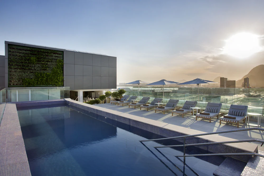 Fachada do DOM Barra Hotel: prédio de quatro andares revestido de painéis brancos, com jardim e acesso coberto na entrada